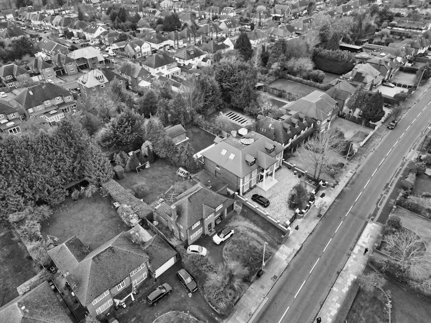 An aerial view of a residential neighborhood in Harlesden, showing closely packed terraced houses with varied roof styles, some covered in light snow or frost, alongside narrow streets lined with park